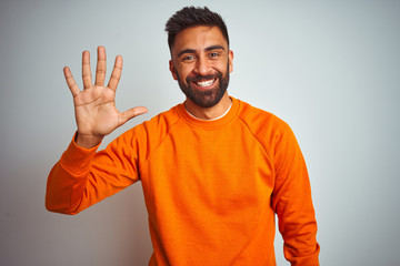 Wall Mural - Young indian man wearing orange sweater over isolated white background showing and pointing up with fingers number five while smiling confident and happy.