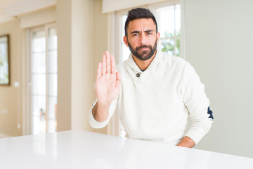 Poster - Handsome hispanic man wearing casual white sweater at home doing stop sing with palm of the hand. Warning expression with negative and serious gesture on the face.