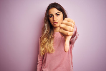 Poster - Young beautiful woman wearing a sweater over pink isolated background looking unhappy and angry showing rejection and negative with thumbs down gesture. Bad expression.