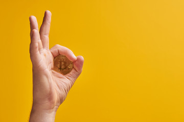 Hand with physical coin bitcoin on yellow background, gesture 