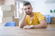 © Krakenimages.com - Young man sitting on the table with cardboard boxes behind him moving to new home thinking looking tired and bored with depression problems with crossed arms.