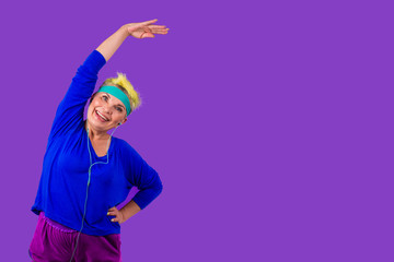 happy active pensioner woman with stylish yellow dyed hair and a blue bandage on forehead after pilates training smiling in studio violet background copy spase