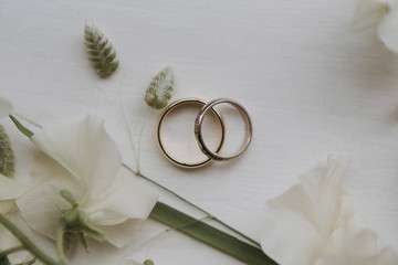 Wall Mural - overhead closeup shot of wedding rings on a white surface decorated with white and green flowers