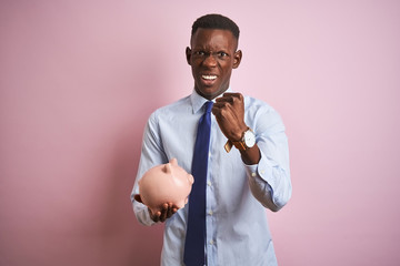 African american businessman holding piggy bank standing over isolated pink background annoyed and frustrated shouting with anger, crazy and yelling with raised hand, anger concept