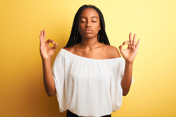 Young african american woman wearing white t-shirt standing over isolated yellow background relax and smiling with eyes closed doing meditation gesture with fingers. Yoga concept.