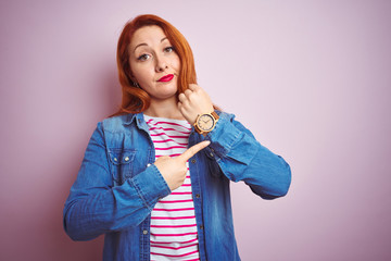 Sticker - Beautiful redhead woman wearing denim shirt and striped t-shirt over isolated pink background In hurry pointing to watch time, impatience, looking at the camera with relaxed expression