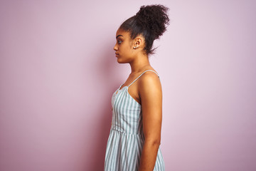 African american woman wearing casual striped dress standing over isolated pink background looking to side, relax profile pose with natural face with confident smile.