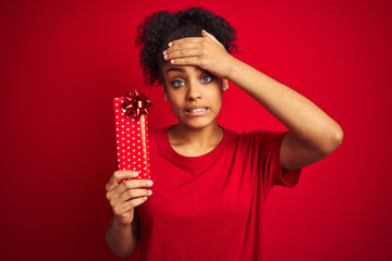 Young african american woman holding valentine gift over isolated red background stressed with hand on head, shocked with shame and surprise face, angry and frustrated. Fear and upset for mistake.