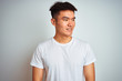 © Krakenimages.com - Young asian chinese man wearing t-shirt standing over isolated white background looking away to side with smile on face, natural expression. Laughing confident.