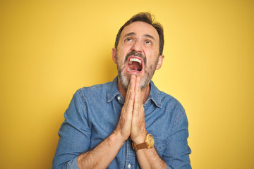 Sticker - Handsome middle age senior man with grey hair over isolated yellow background begging and praying with hands together with hope expression on face very emotional and worried. Asking for forgiveness. 