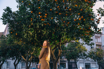 Wall Mural - girl in a dress on the sidewalk waving her hair. trees with oran