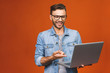 © denis_vermenko - Indoor portrait of young man in casual standing against orange backgroundl with copy space for ads, holding laptop, smiling.