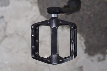 one black pedal on a bicycle on a background of gray asphalt