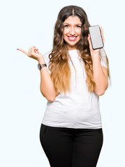 Sticker - Young adult woman showing smartphone screen very happy pointing with hand and finger to the side