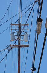 Electricity distribution pylon with wiring cables and electrical equipment seen against a bright blue sky