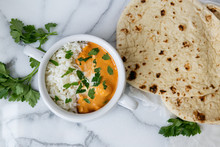 Top View Of Indian Butter Chicken With Jasmine Rice, Fresh Baked Naan, Topped With Cilantro, Marble Background