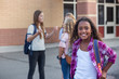© Brocreative - Cute, diverse pre-adolescent teen student hanging out with friends after school. Selective focus on the smiling girl student standing outside the school building