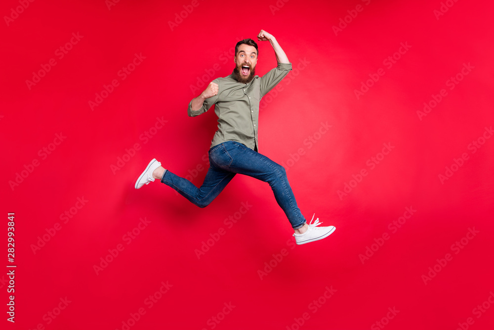 Full length body photo of bearded strong sporty handsome white man wearing grey t-shirt running somewhere with victory while isolated with red background - obrazy, fototapety, plakaty 