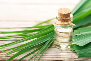 Wall Mural - lemongrass essential oil in the bottle, with fresh lemongrass leaves, on the wooden table