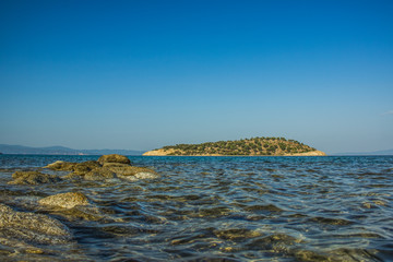 Wall Mural - south European Mediterranean sea scenery landscape view of stones and wavy water foreground and island shoreline background 