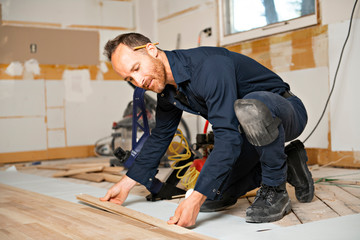 a male worker install wood floor on a house