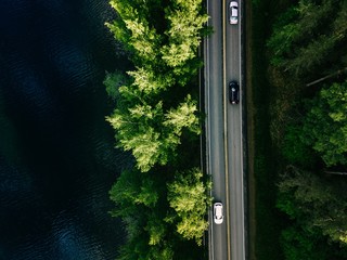 Aerial landscape view of road between green pine forest and blue lake in Finland