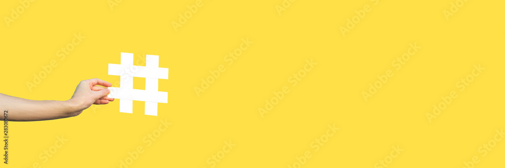 Social media concept. closeup of human hand holding and showing large big white hashtag sign. indoor studio shot, isolated on yellow background copyspace. marketing symbol, instagram followers. - obrazy, fototapety, plakaty 