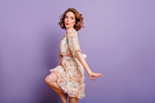Inspired European Young Woman Dancing In Studio And Laughing. Winsome Brunette Girl In Cute Dress Jumping On Purple Background.