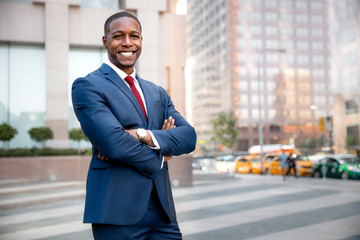 Proud successful businessman executive CEO african american, standing confidently with arms folded in downtown, financial buildings and skyscrapers