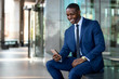 © elnariz - African american businessman smiling cheerful, using cell phone at office building, internet, broadband, 5G, copy space
