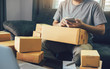 © wutzkoh - Asian young man using smart phone for checking shipment at home.