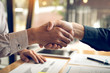 © wutzkoh - Entrepreneurs collaboration deal shaking hands in a modern office and financial paper graph on desk.
