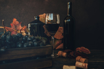 Wall Mural - Red wine tasting in the winery. Full wine glass next to a vintage box and lush vine leaves on the background, winemaking concept. Toned image. Selective focus.