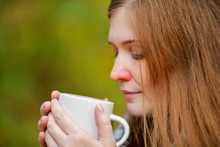 Close Up. Girl With A Red Nose Drinking Hot Tea From A White Mug. Cold Girl. The Girl Is Sick With A Runny Nose Drinking Cure. Redheaded Woman. Horizontal Photography