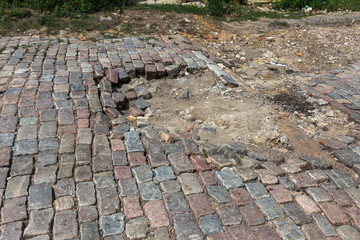 Canvas Print - Damaged asphalt road with potholes, caused by freeze-thaw cycles in winter. Bad road. Broken pavements sidewalks on sidewalk. pavement with paving slabs with defects and cracks coming in perspective