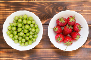 Natural organic homegrown products concept. Red ripened strawberries and green gooseberries in white bowls.