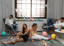 Group Of Friends Suffering From Hangover In Messy Room After Party