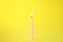 Burning Pink Striped Birthday Candle On Yellow Background