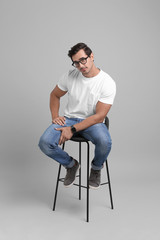 Wall Mural - Handsome young man sitting on stool against grey background