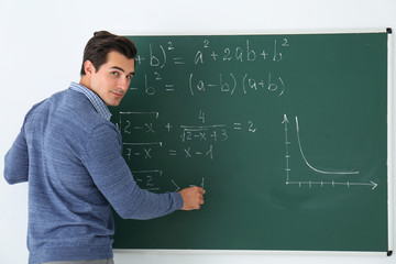 Young teacher writing math formulas on chalkboard in classroom