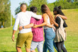 © Mangostar - Back view of friends hugging while strolling on meadow. Young people talking while walking together. Friendship concept