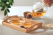 A hand pouring tea from glass teapot on wooden serving tray