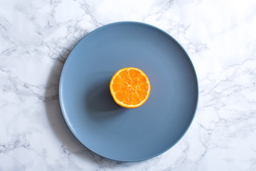 Half of orange on the blue plate on the marble background