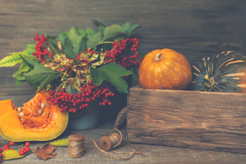 Wall Mural - Autumn background with red berries with green leaves, pumpkins in the vintage wooden box. Fall harvest on aged wood with copy space. Mockup for seasonal offers and holiday post card. Toned image.