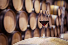 Closeup Glass With Red Wine On Background Wooden Wine Oak Barrel Stacked In Straight Rows In Order, Old Cellar Of Winery, Vault. Concept Professional Degustation, Winelover, Sommelier Travel