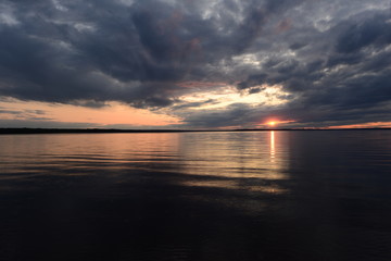 Wall Mural - Rays of the sun in a moody rainy cloudy sky with a reflection on the surface of the water