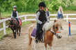 © Dusan Petkovic - Children with helmets and protective vests on riding pony horses at sunny day on ranch.