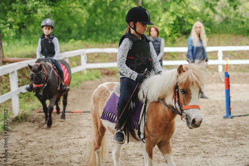 Cuadros en Lienzo Children with helmets and protective vests on riding pony horses at sunny day on ranch