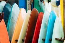 Close Up Set Of Colorful Surfboard For Rent On The Beach. Multicolored Surf Boards Different Sizes And Colors Surfing Boards On Stand, Surfboards Rental Place