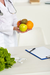 Wall Mural - partial view of dietitian in white coat holding fresh fruits near workplace